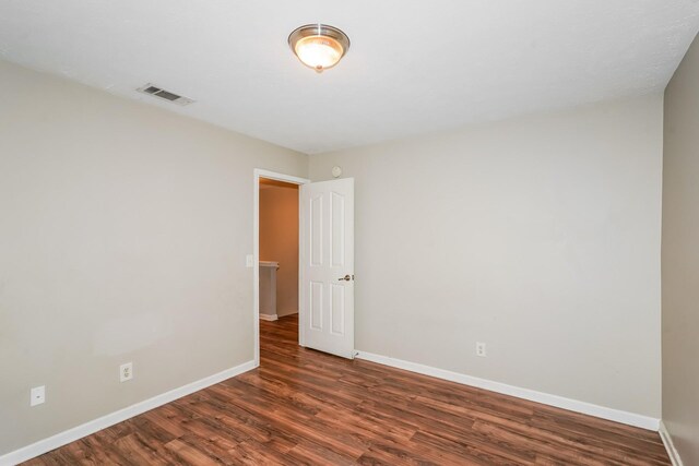 unfurnished room featuring visible vents, dark wood-type flooring, and baseboards