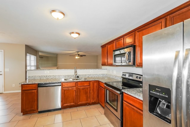 kitchen featuring light tile patterned floors, light stone countertops, a peninsula, a sink, and stainless steel appliances