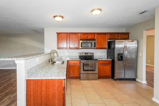 kitchen featuring light stone counters, visible vents, a peninsula, a sink, and appliances with stainless steel finishes