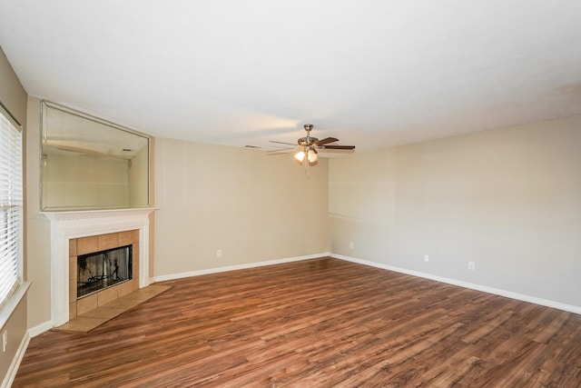 unfurnished living room featuring a tiled fireplace, baseboards, and wood finished floors