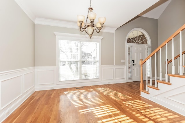 foyer featuring stairway, wood finished floors, crown molding, and a chandelier