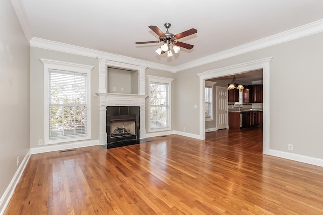 unfurnished living room featuring a wealth of natural light, wood finished floors, a tiled fireplace, and crown molding