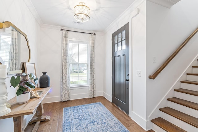 foyer featuring wood finished floors, baseboards, stairs, crown molding, and a notable chandelier