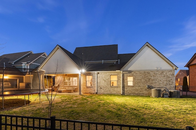 rear view of property featuring a lawn, a patio, a trampoline, fence, and brick siding