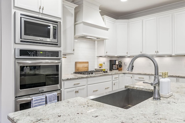 kitchen featuring premium range hood, decorative backsplash, white cabinets, stainless steel appliances, and a sink