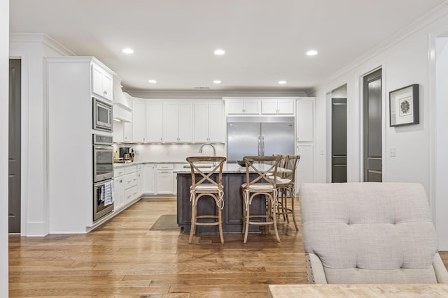 kitchen with built in appliances, a breakfast bar area, white cabinetry, and light wood-style floors