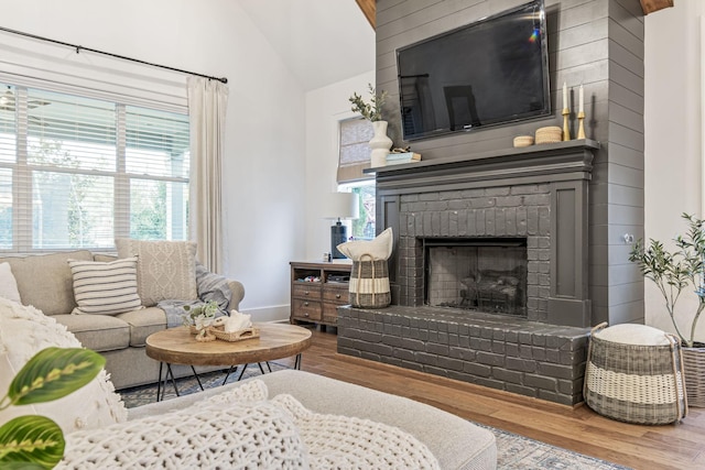 living area featuring a fireplace, wood finished floors, baseboards, and vaulted ceiling