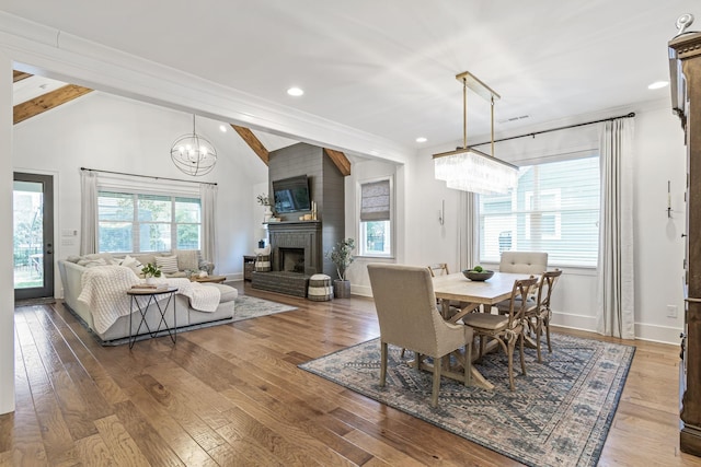 dining space with hardwood / wood-style floors, a fireplace, baseboards, a chandelier, and vaulted ceiling with beams