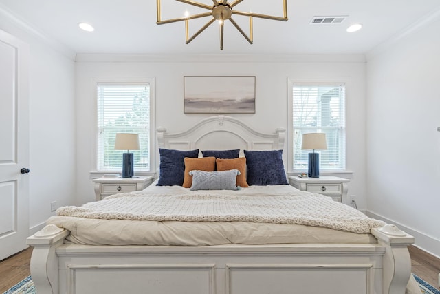 bedroom with wood finished floors, visible vents, baseboards, an inviting chandelier, and crown molding