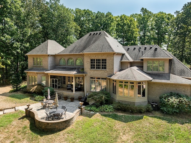 back of property with a patio, a lawn, brick siding, and roof with shingles