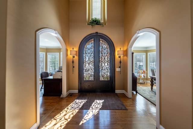 entrance foyer featuring arched walkways, baseboards, and wood finished floors