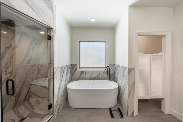 full bathroom featuring a marble finish shower, a soaking tub, tile walls, and wainscoting