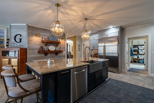 kitchen featuring light stone counters, a center island with sink, arched walkways, a sink, and appliances with stainless steel finishes