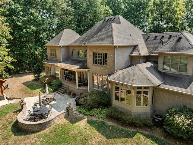 back of house with a patio area, brick siding, roof with shingles, and a sunroom