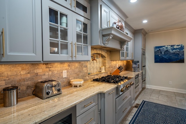 kitchen with light stone countertops, baseboards, glass insert cabinets, appliances with stainless steel finishes, and tasteful backsplash