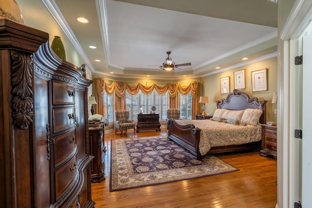 bedroom with recessed lighting, a tray ceiling, wood finished floors, and crown molding