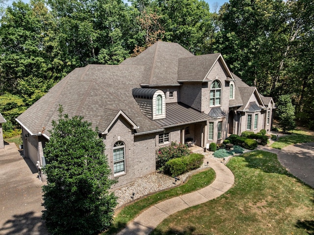 view of front of home featuring a standing seam roof, a shingled roof, a front lawn, brick siding, and metal roof