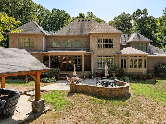 back of property with a yard, brick siding, roof with shingles, and a patio area