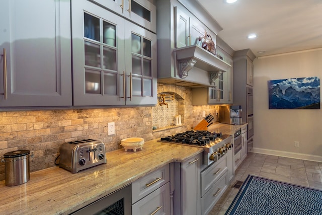 kitchen with glass insert cabinets, baseboards, light stone countertops, decorative backsplash, and stainless steel gas stovetop