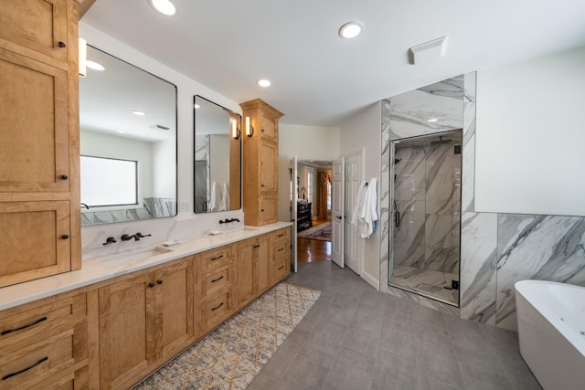 bathroom featuring a marble finish shower, double vanity, a freestanding tub, recessed lighting, and a sink