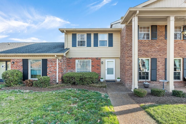 townhome / multi-family property featuring a front lawn, brick siding, and roof with shingles