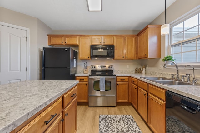 kitchen with brown cabinets, black appliances, light wood-style flooring, a sink, and decorative light fixtures