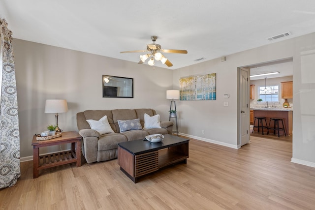 living room with light wood-style flooring, baseboards, visible vents, and ceiling fan