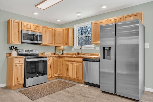 kitchen featuring light wood-style flooring, light brown cabinets, a sink, stainless steel appliances, and light countertops