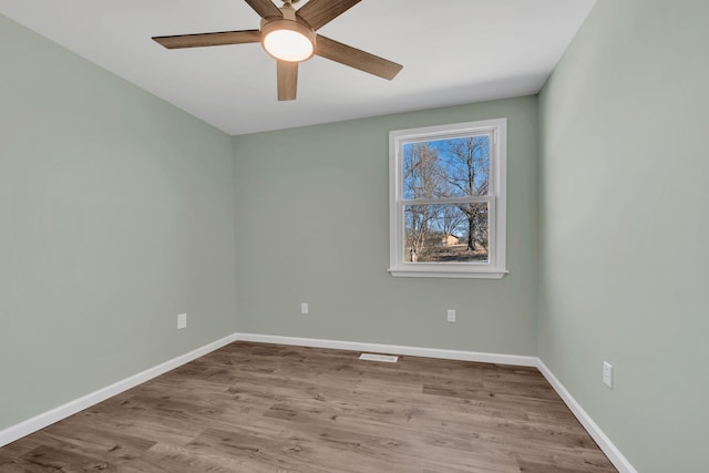 spare room featuring ceiling fan, visible vents, baseboards, and wood finished floors