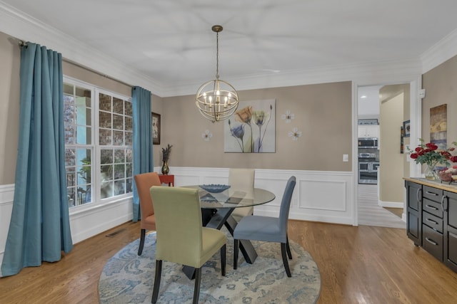 dining area with a wainscoted wall, visible vents, light wood-style floors, crown molding, and a chandelier