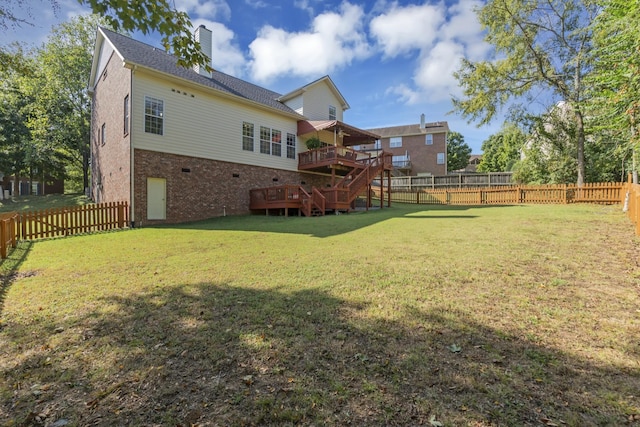 back of house featuring a yard, a fenced backyard, a chimney, a deck, and brick siding