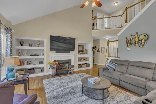 living area with stairway, built in shelves, a ceiling fan, wood finished floors, and a fireplace with flush hearth