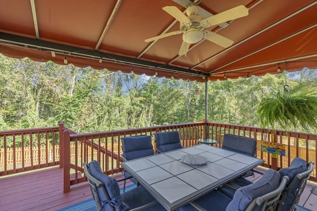 wooden terrace with ceiling fan, a view of trees, and outdoor dining space