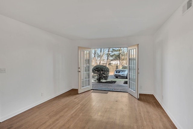 unfurnished room with wood finished floors, french doors, visible vents, and baseboards