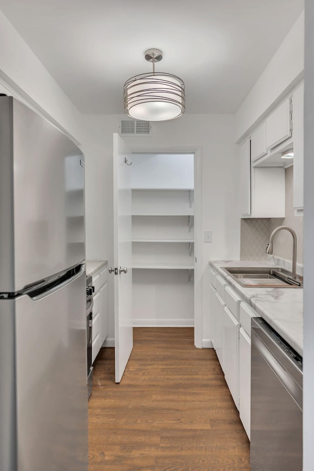 kitchen featuring visible vents, a sink, stainless steel appliances, dark wood-type flooring, and light countertops