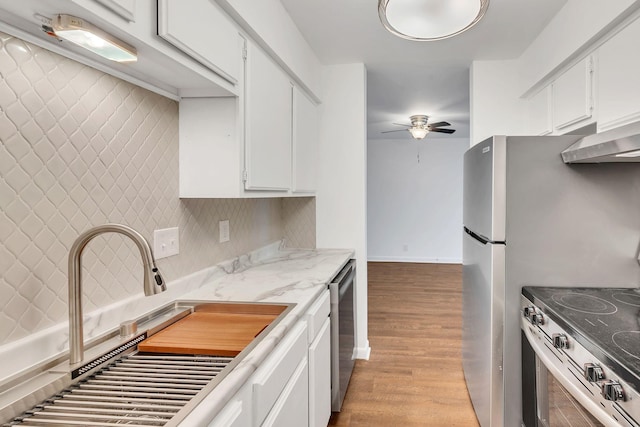 kitchen featuring a ceiling fan, light wood finished floors, a sink, decorative backsplash, and stainless steel appliances