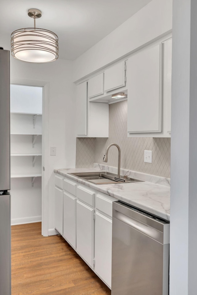 kitchen with light wood finished floors, tasteful backsplash, white cabinets, stainless steel appliances, and a sink