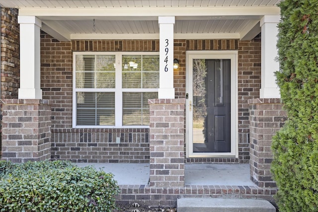 doorway to property featuring a porch and brick siding