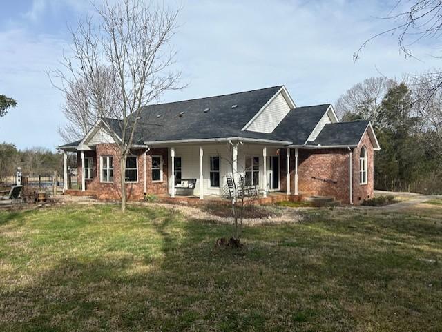 rear view of property with brick siding, covered porch, and a lawn