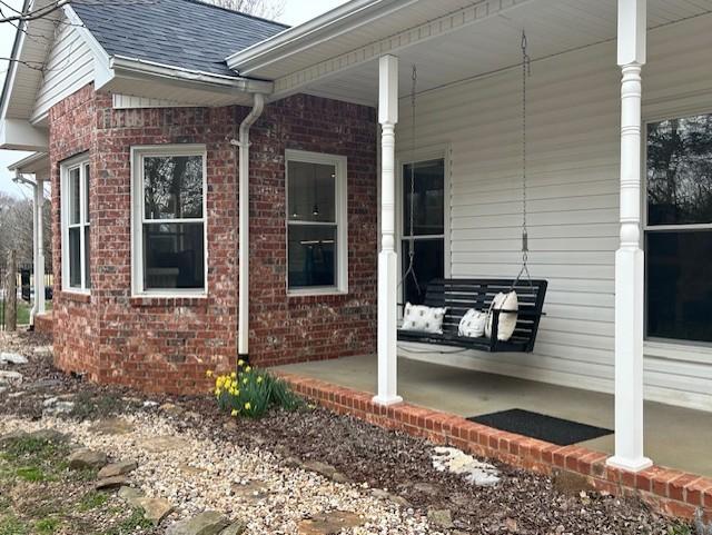 view of side of property featuring brick siding, covered porch, and roof with shingles