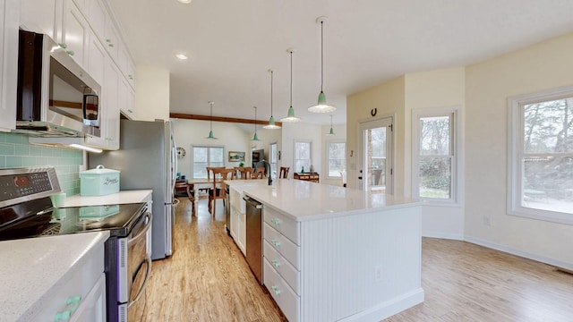 kitchen with backsplash, white cabinetry, stainless steel appliances, light wood finished floors, and light countertops