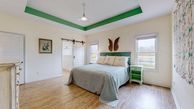 bedroom featuring a tray ceiling, a barn door, multiple windows, and wood finished floors