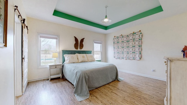 bedroom featuring light wood-style flooring, a raised ceiling, baseboards, and multiple windows