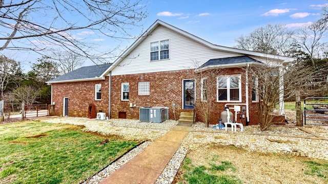 rear view of house with brick siding, central air condition unit, fence, and a gate