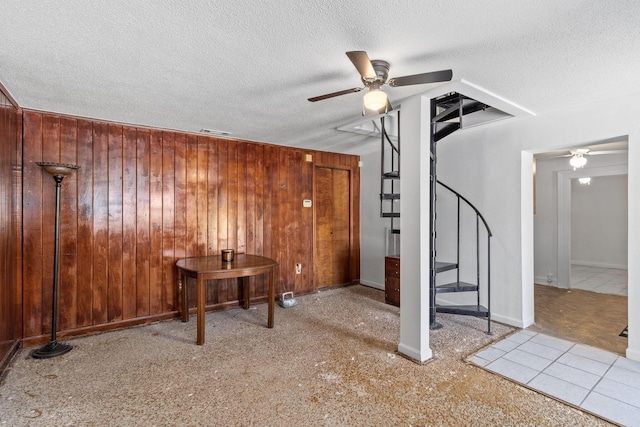 interior space with visible vents, wooden walls, ceiling fan, stairway, and a textured ceiling