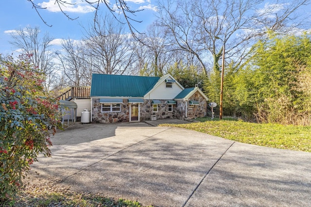 chalet / cabin with stone siding, concrete driveway, metal roof, and a front yard