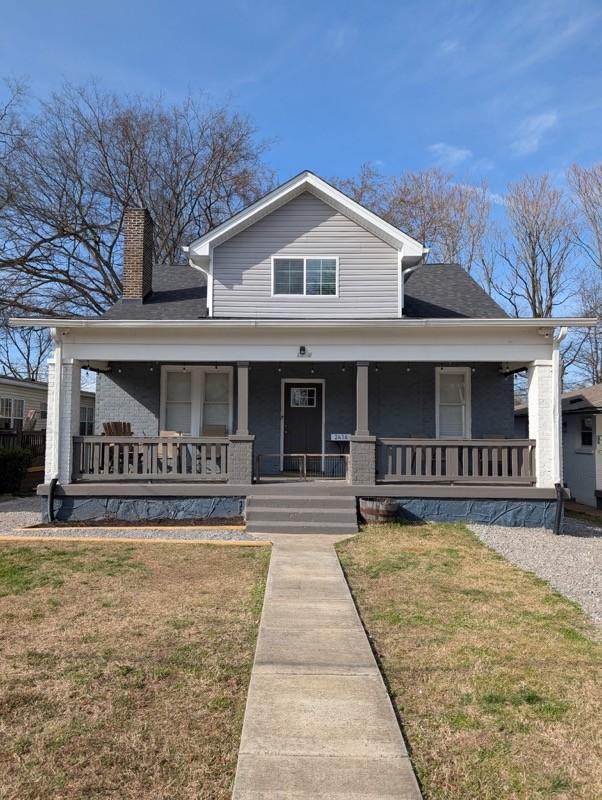 view of front of property featuring covered porch, a chimney, and a front yard