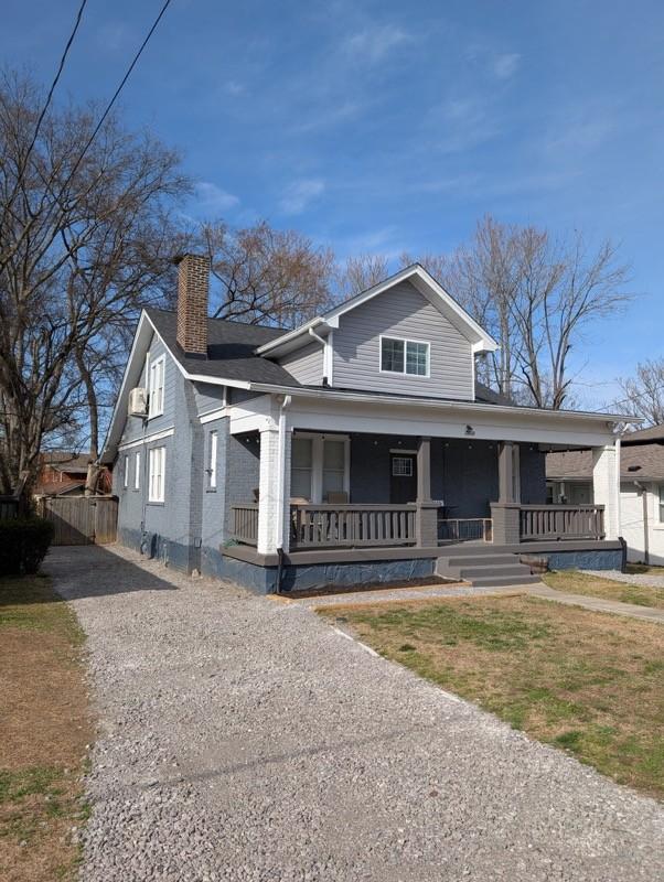 view of front facade with a porch, brick siding, driveway, and a chimney