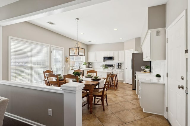 kitchen featuring backsplash, white cabinetry, stainless steel appliances, light countertops, and hanging light fixtures