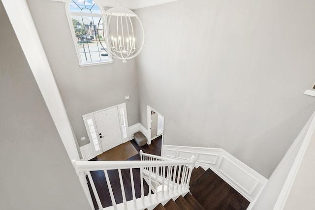 staircase with a wainscoted wall, wood finished floors, a high ceiling, an inviting chandelier, and a decorative wall